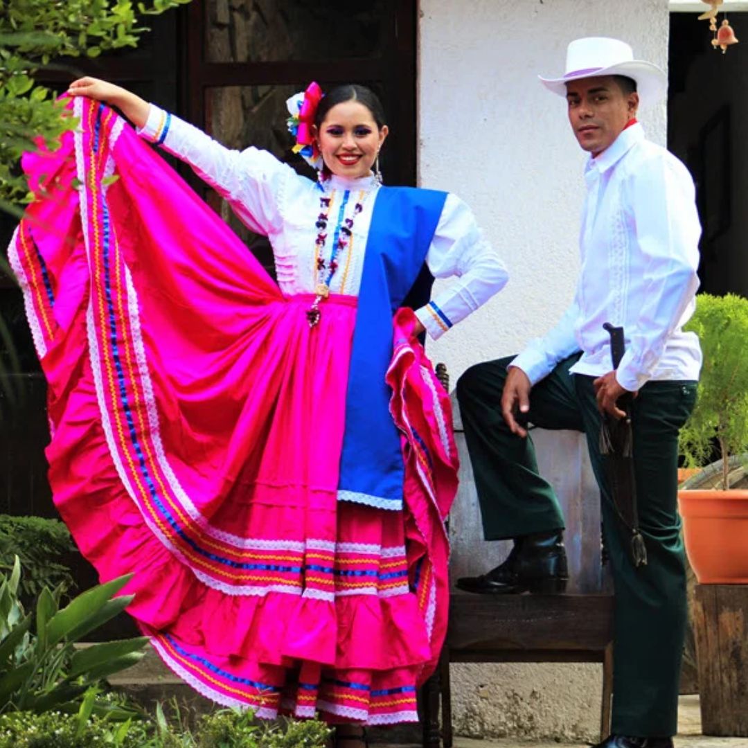 Vestido típico rosado con accesorios de flores y traje de varón con camisa blanca y pantalón negro.