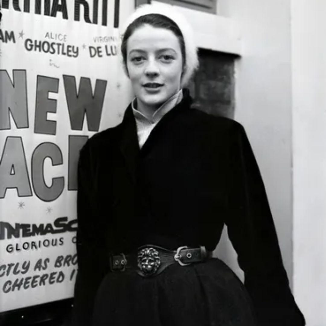 Maggie Smith de joven con un traje negro y faja a la moda.