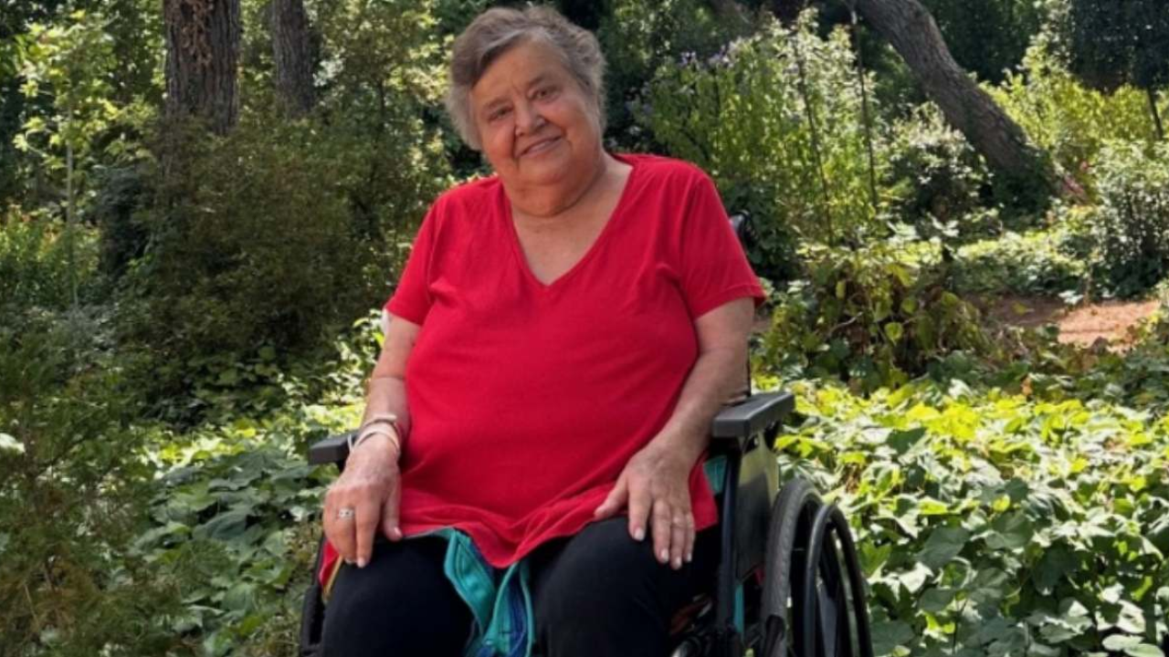 Cristina con una blusa roja, sentada en una silla de ruedas color negro.
