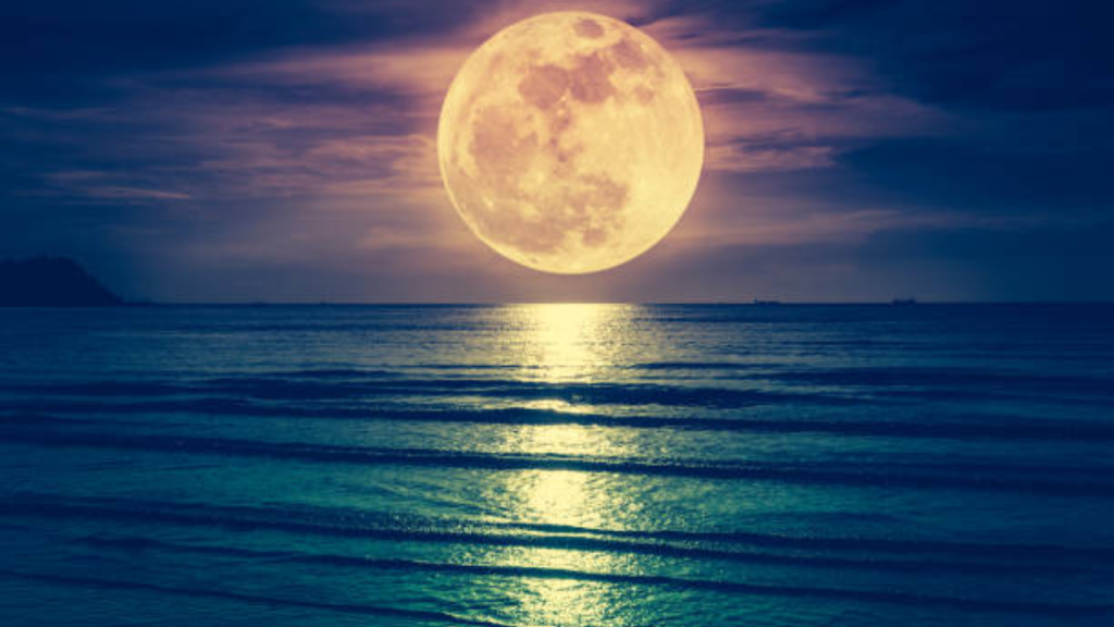 Imagen de la luna color amarilla a la vista del mar azul.