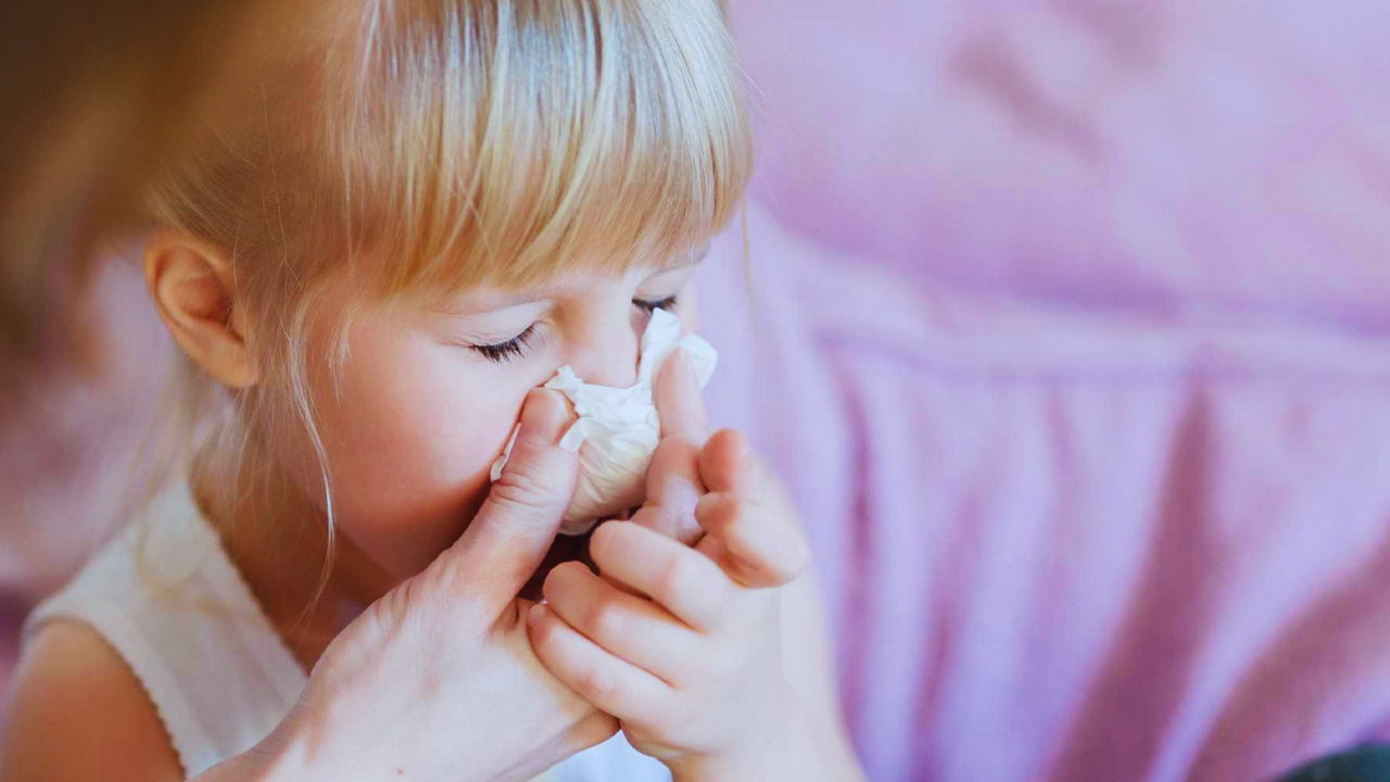 Una niña con cabello rubio y blusa escotada blanca con gripe.