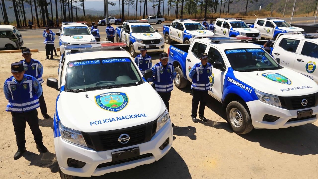 Agentes de policía con su uniforme azul y blanco, junto a carros de la institución color azul y blanco.