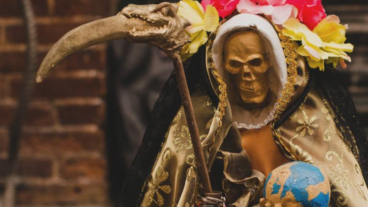 Imagen de la Santa Muerte negra decorada con flores color rosa y amarillo.