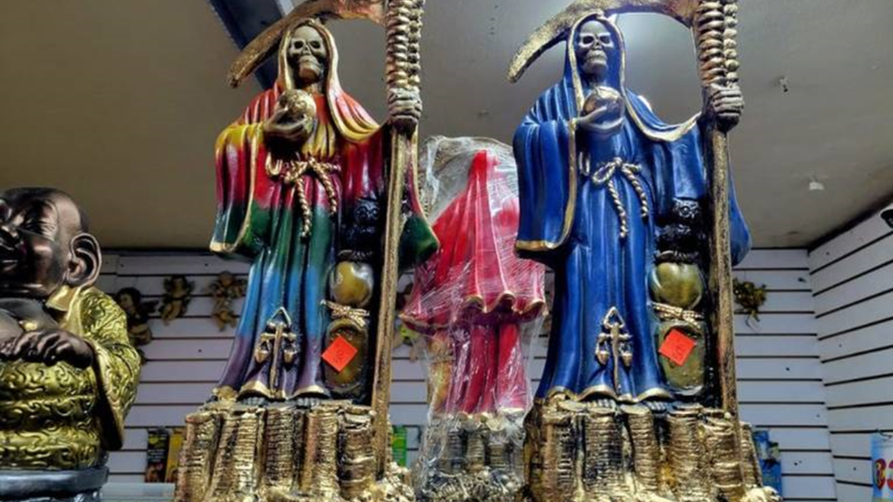 Dos figuras de la Santa Muerte negra, una de colores y otra azul, con el mundo en sus manos, la guadaña y la balanza.

