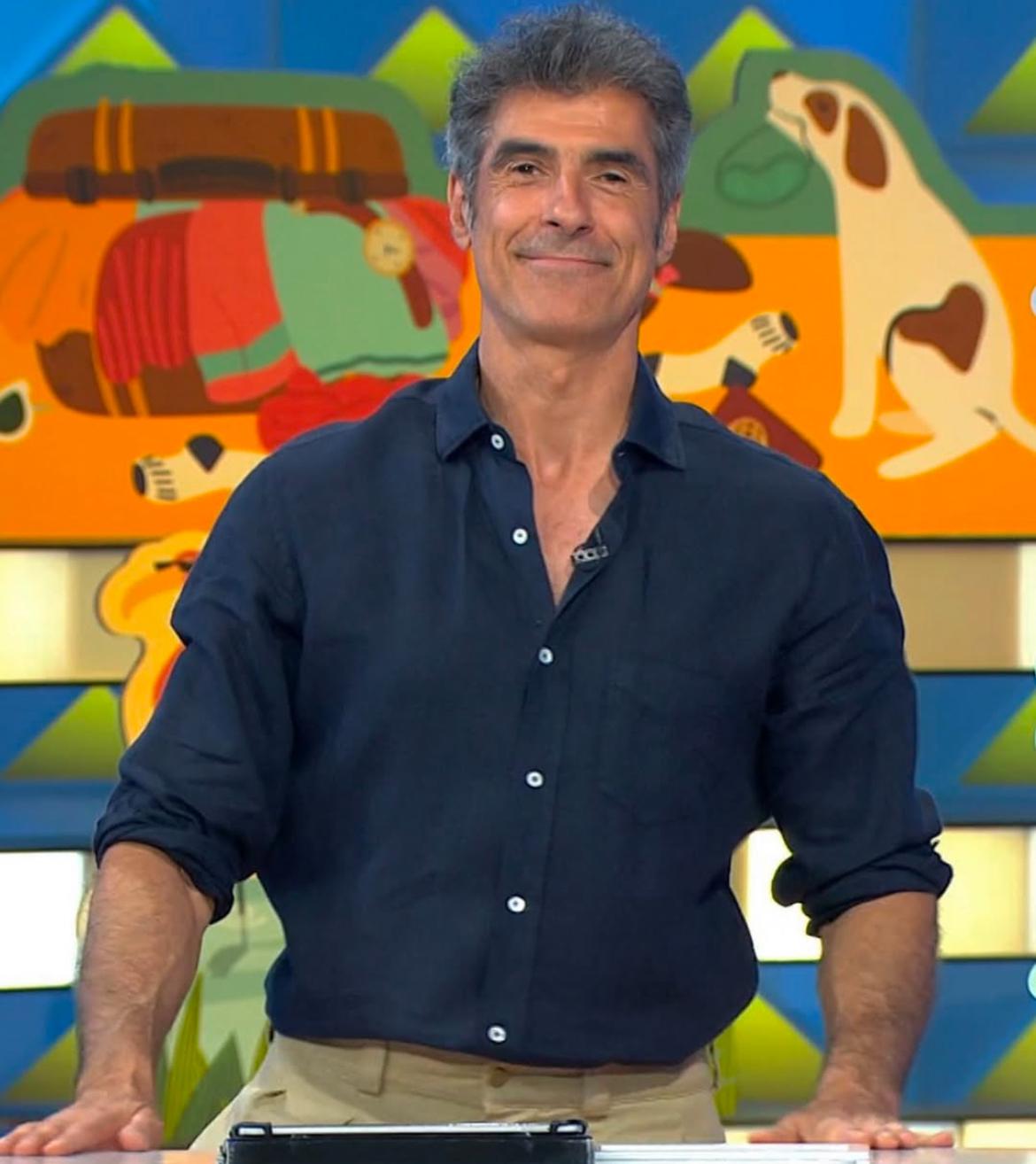 Presentador de televisión Jorge Fernández, utilizando una camisa azul marino con botones y fondo colorido