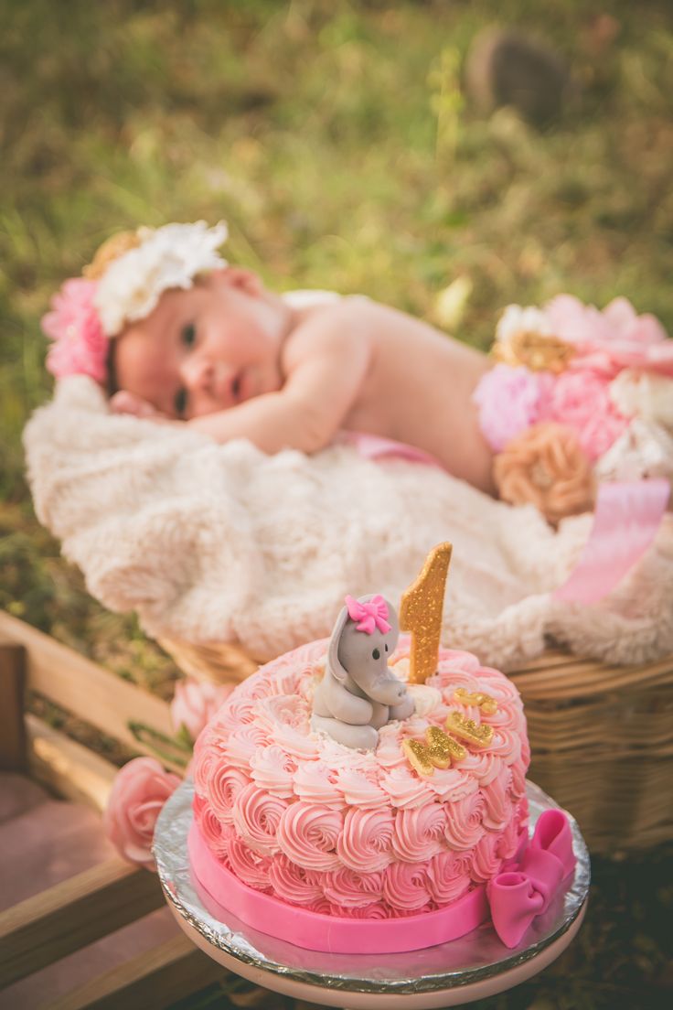 Un pastel con número 1 y un recién nacido al fondo.