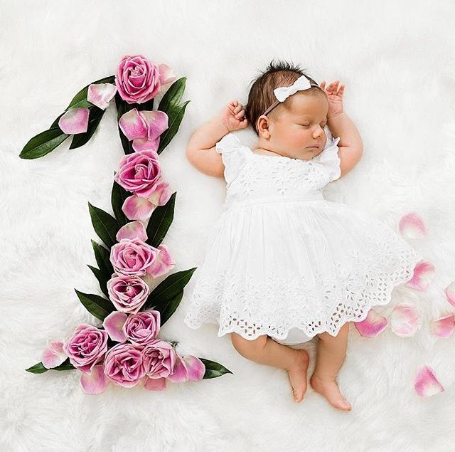 Una recién nacida junto a un número uno hecho a base de flores