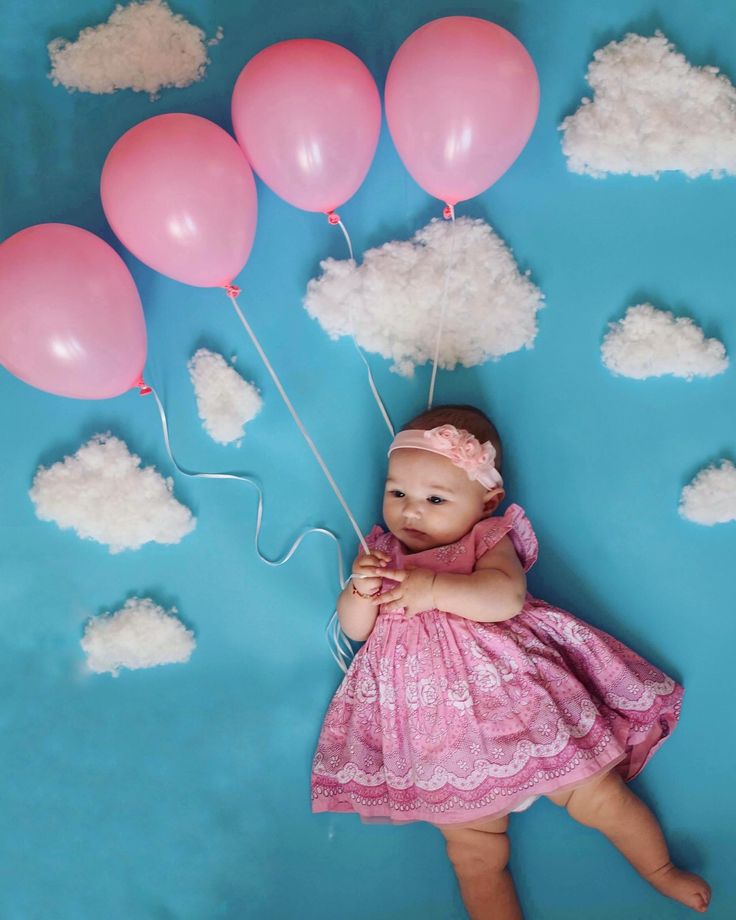 Una bebé con un vestido rosado con cuatro globos rosados