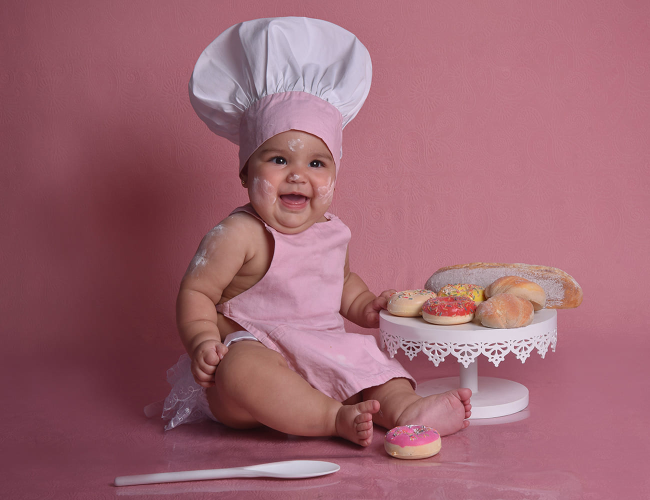 Una niña vestida de panadera junto a donas y pan.