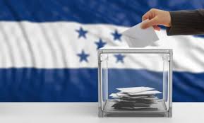 La bandera de Honduras al fondo y enfrente una mano votando. Elecciones primarias Honduras.