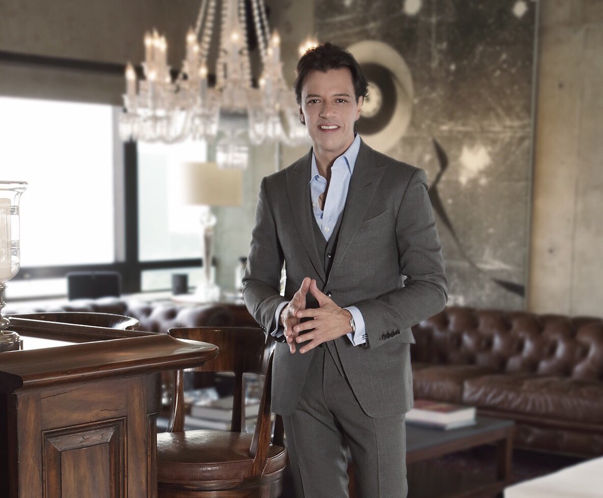 Rodrigo Herrera con traje y cruzando las manos dentro de una casa