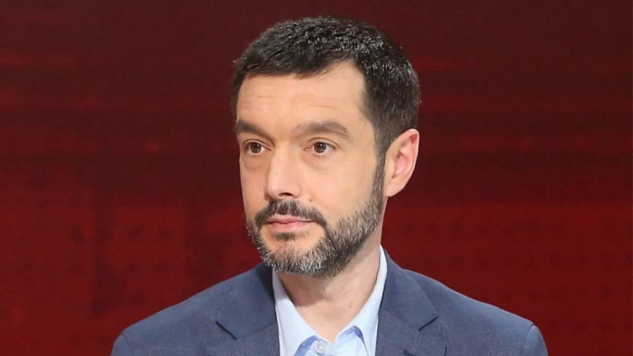 Pablo Bustinduy vestido de saco y camisa de botones y un fondo rojo.