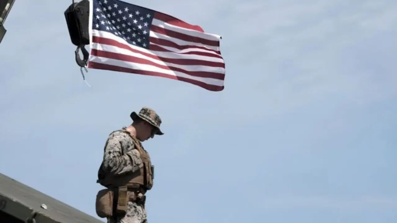 Fotografía de militar junto a la bandera de Estados Unidos.