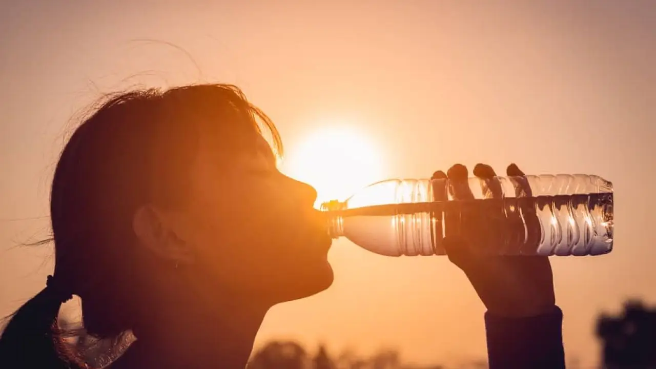 Una mujer toma agua mientras camina bajo un fuerte sol 
