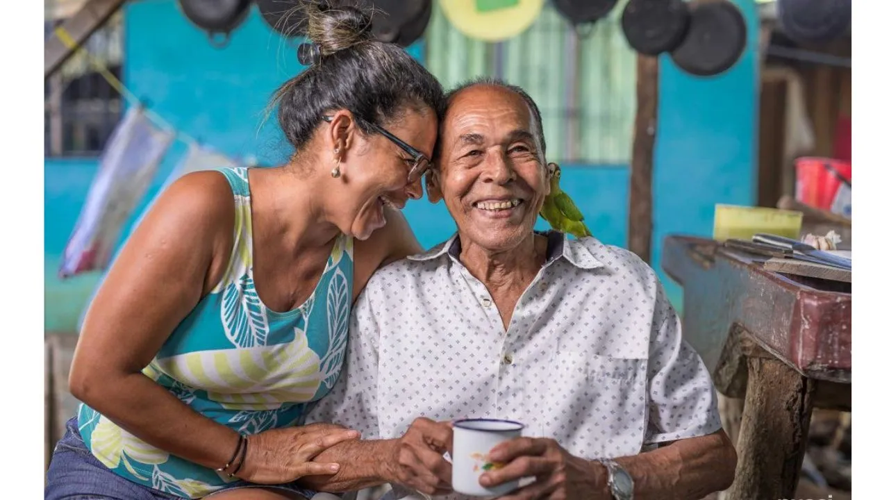 Una pareja sonriendo junto, el señor con una taza de café en su mano, mientras tiene una mascota en sus hombros.