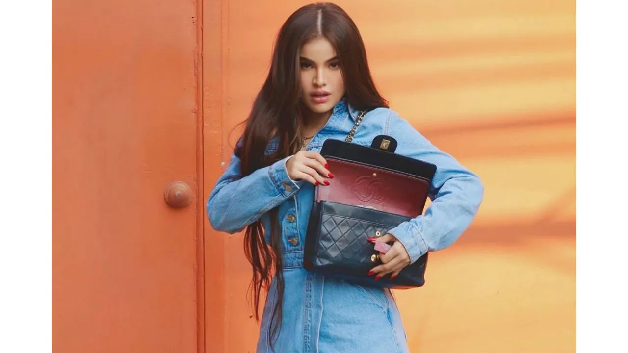 Graden con un vestido azul, de cabello largo y sosteniendo un bolso de color negro.