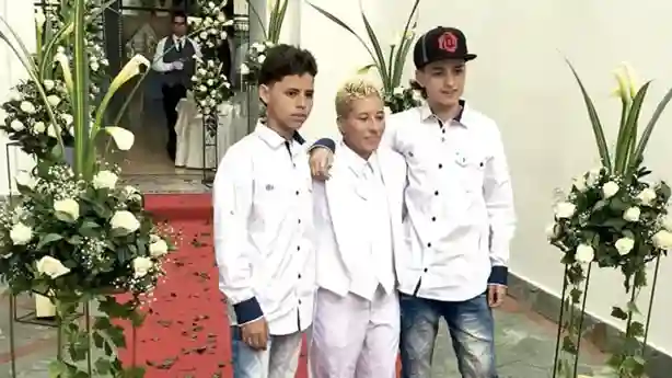 Lady a la par de sus hijos abrazándolos vestida de color blanco.