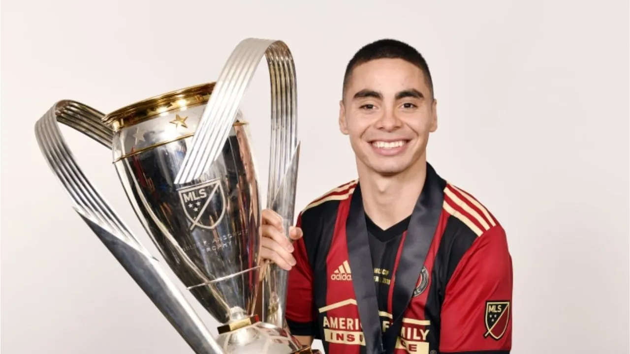 Almiron sostiene un trofeo con sus manos, con una camisa deportiva de color rojo con negro.