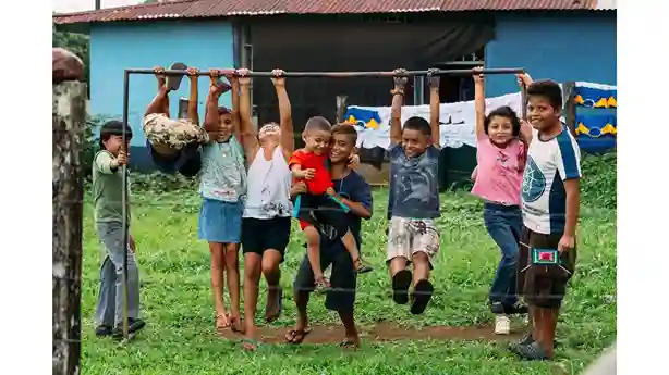 Niños juegan con las manos extendidas hacia un tubo.
