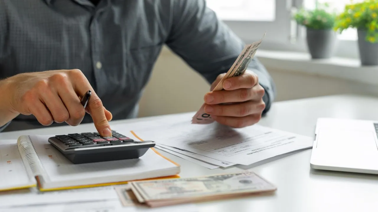 Un joven hará un préstamo de su dinero al Gobierno, está sacando sus cuentas con una calculadora.