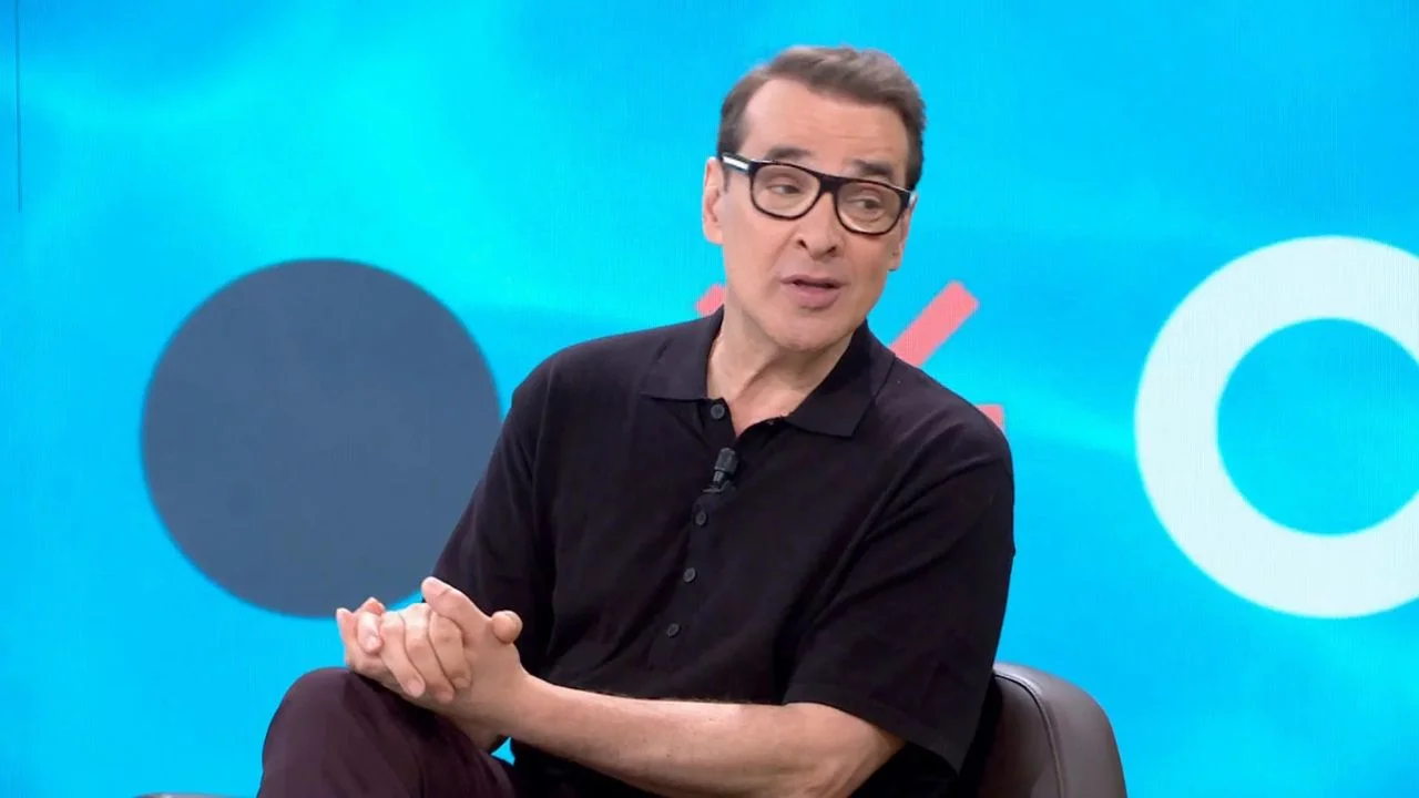 Luis Merlo con una camisa negra y gafas en un programa de televisión.