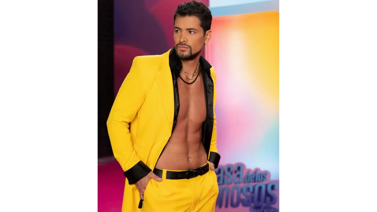 Moisés posa con su traje color amarillo, mientras tiene sus manos en la bolsa de su pantalón, con una mirada fija.