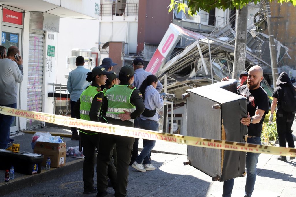 Un hombre recoge pertenencias en una zona custodiada por policías frente a una edificación destruida