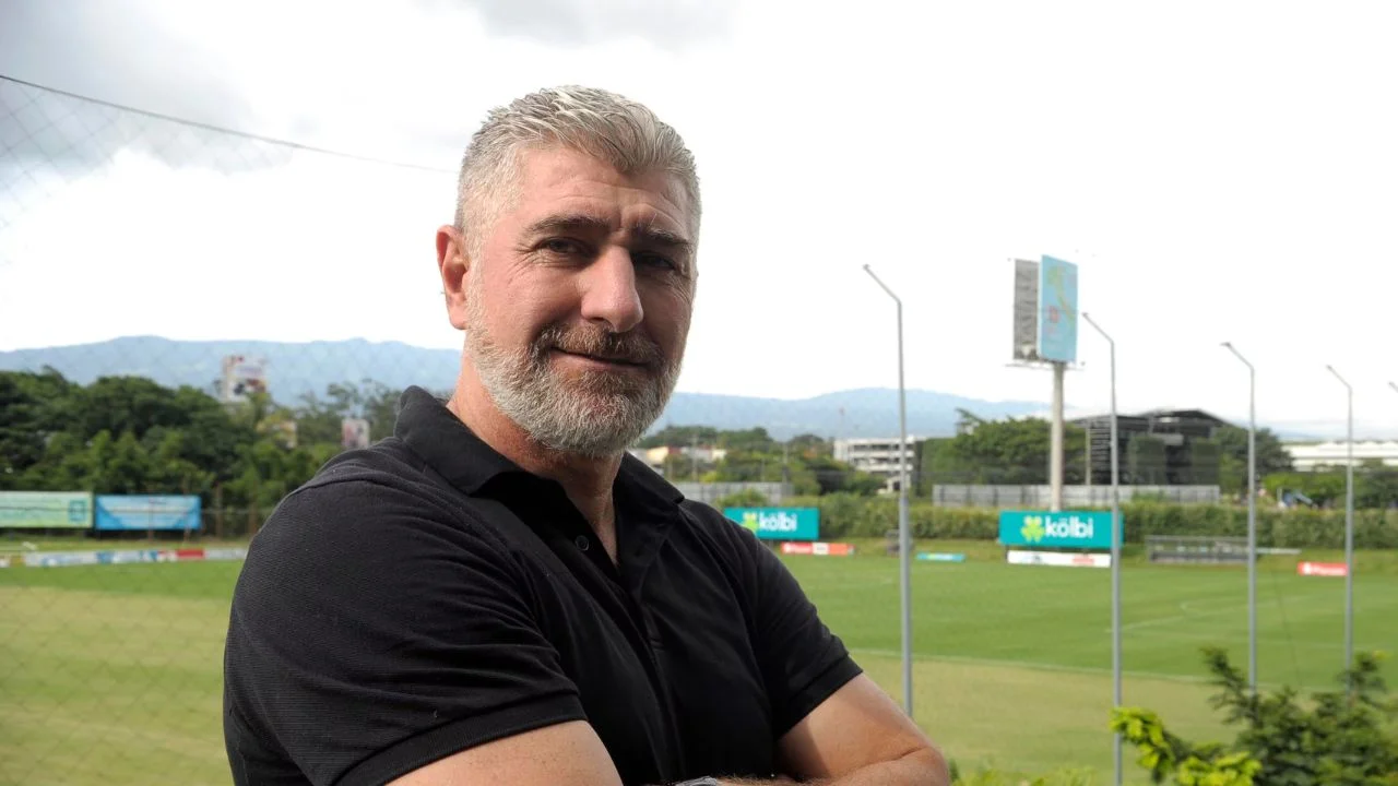 Alejandro Larrea vestido de negro y con una cancha de fútbol del fondo.