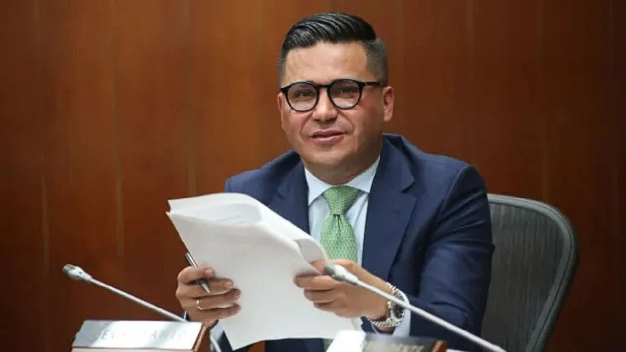 Jorge Eliécer con traje y corbata y con unos papeles en mano.