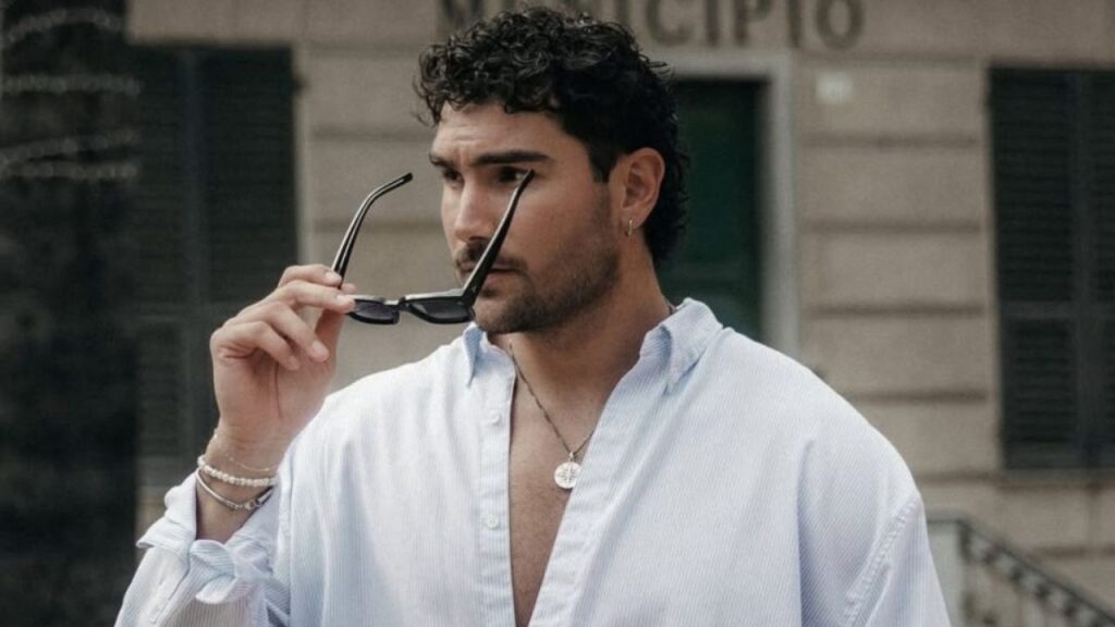 Kenzo exjugador de baloncesto posa para una fotografía con sus lentes, camisa blanca y una cadena. 