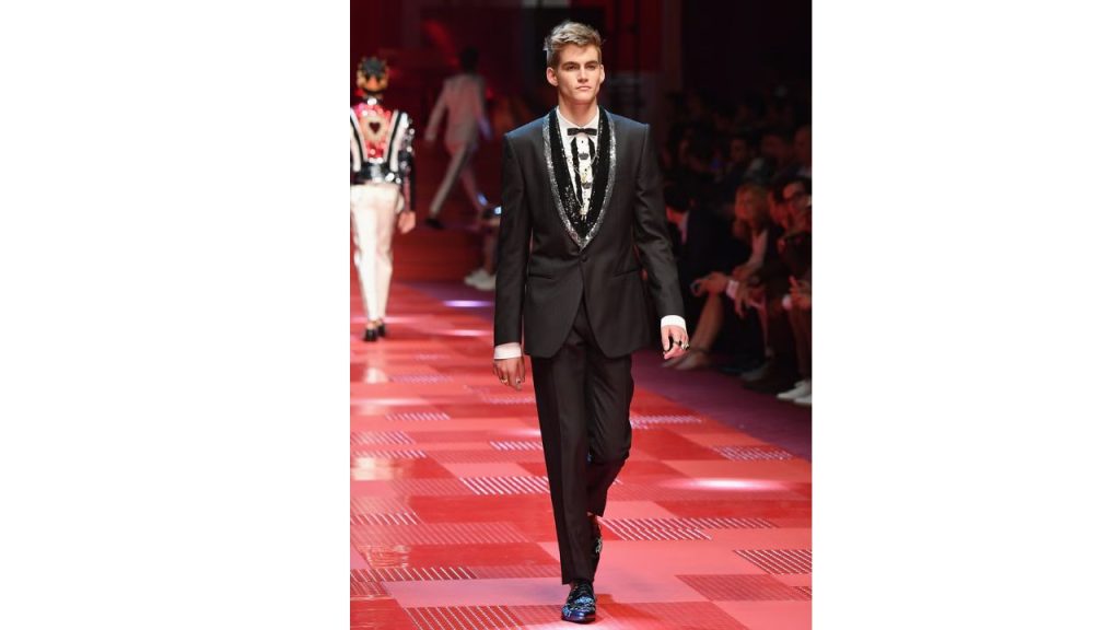 Modelo luce un traje color negro mientras hace una pasarela.