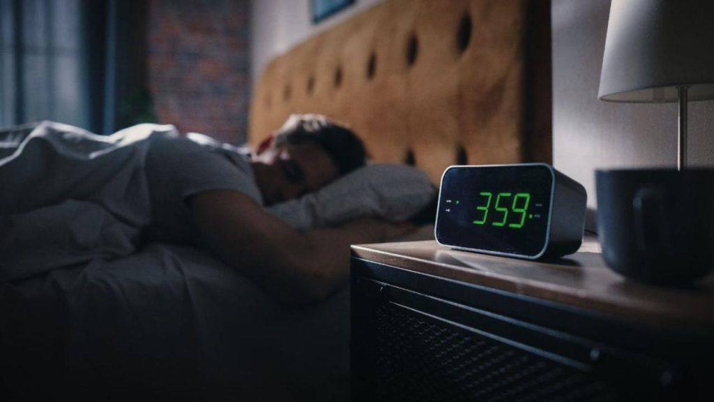 Una persona durmiendo, con reloj a la par de su cama.